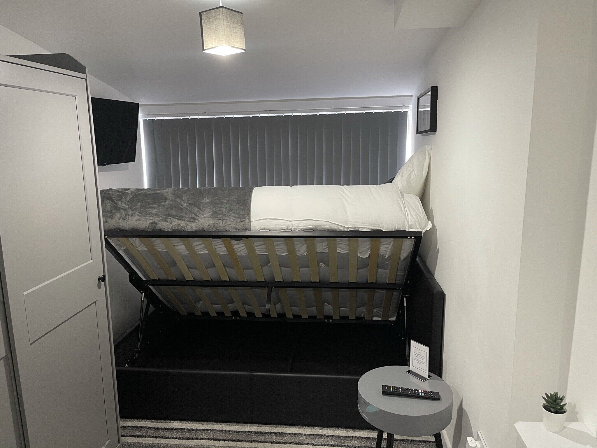 A compact room with a bunk bed, a small round table with a remote control, a potted plant, and a framed picture on the wall.