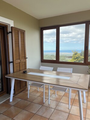 Une table à manger avec des chaises, une vue sur la mer et une porte avec des volets en bois.