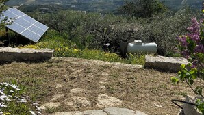A stone pathway leading to a solar panel and a water tank in a rural setting with a view of rolling hills and mountains.