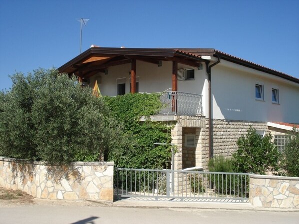 A two-story house with a stone facade, a balcony, and a metal gate.