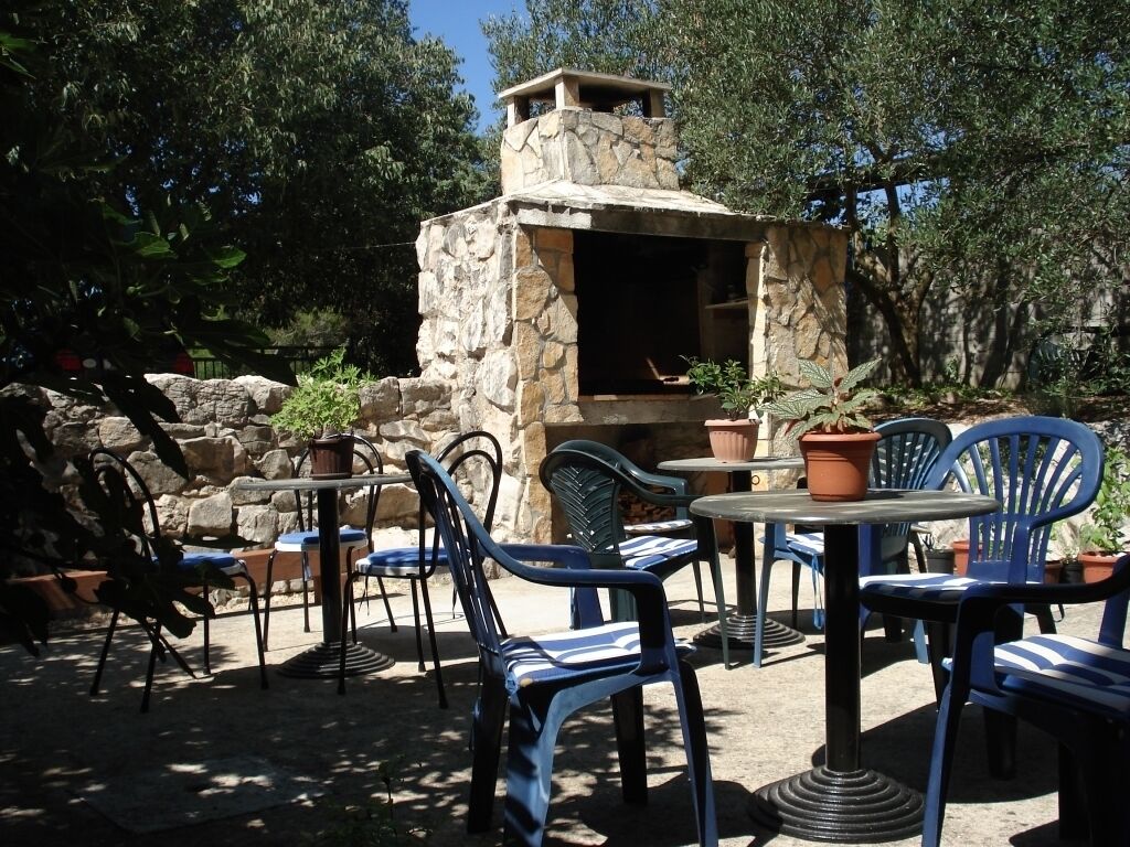 En uteplats med en grillplats av sten, blå stolar och krukväxter.