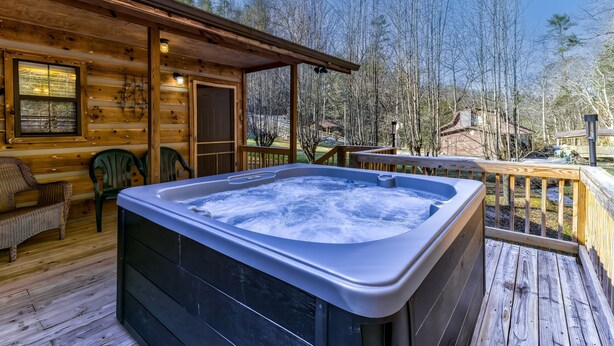 Uma cabana de madeira com hidromassagem em um deck, rodeada por árvores.