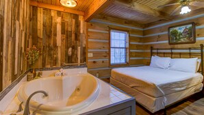 Quarto de cabana de tronco com uma banheira grande, uma cama e um ventilador de teto.