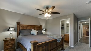 Camera da letto con un letto in legno, due comodini, una ventola a soffitto e vista sul bagno comunicante.