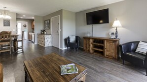 Un ampio soggiorno con un tavolino in legno, un divano in pelle nera e una televisione montata a parete.