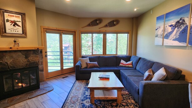 A living room with a stone fireplace, a sofa, a coffee table, and a large window with a view of greenery.