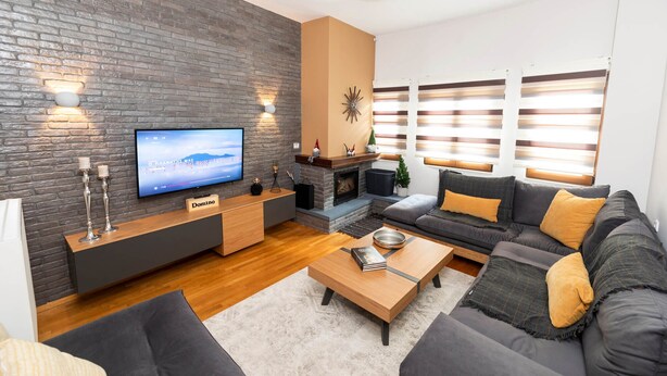 Een moderne woonkamer met een bakstenen muur, een flatscreen televisie, een open haard en een bank met kussens.