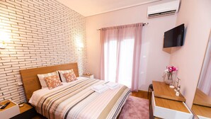 Een moderne slaapkamer met een wand in baksteenmotief, een houten bed, een nachtkastje met lamp, een flatscreen-tv en een groot raam met dunne gordijnen.