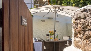 An outdoor seating area with a wicker table, a white umbrella, and a stone wall. - Traditional cosy cottage which lies in the heart of St Agnes (St Agnes)