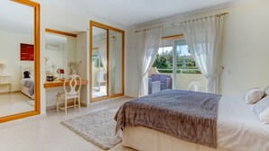 A bedroom with a bed, a desk, a chair, a mirror, and a view of a balcony.