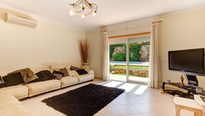 A living room with a sofa, a black rug, a television, and a view of a garden through a sliding glass door.