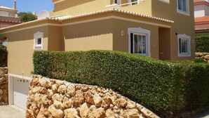 A two-story house with a flat roof, a stone wall in front, and a well-maintained hedge.
