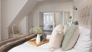 Une chambre avec un grand lit, une table de chevet en bois, une chaise et une vue sur un balcon avec une baignoire.