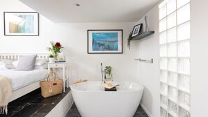 Ein modernes Badezimmer mit einer freistehenden Badewanne, einem weißen Waschtisch und einem Bett mit weißem Kopfteil.