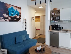 A modern living room with a blue sofa, a coffee table, and a kitchen area with white cabinets and appliances.