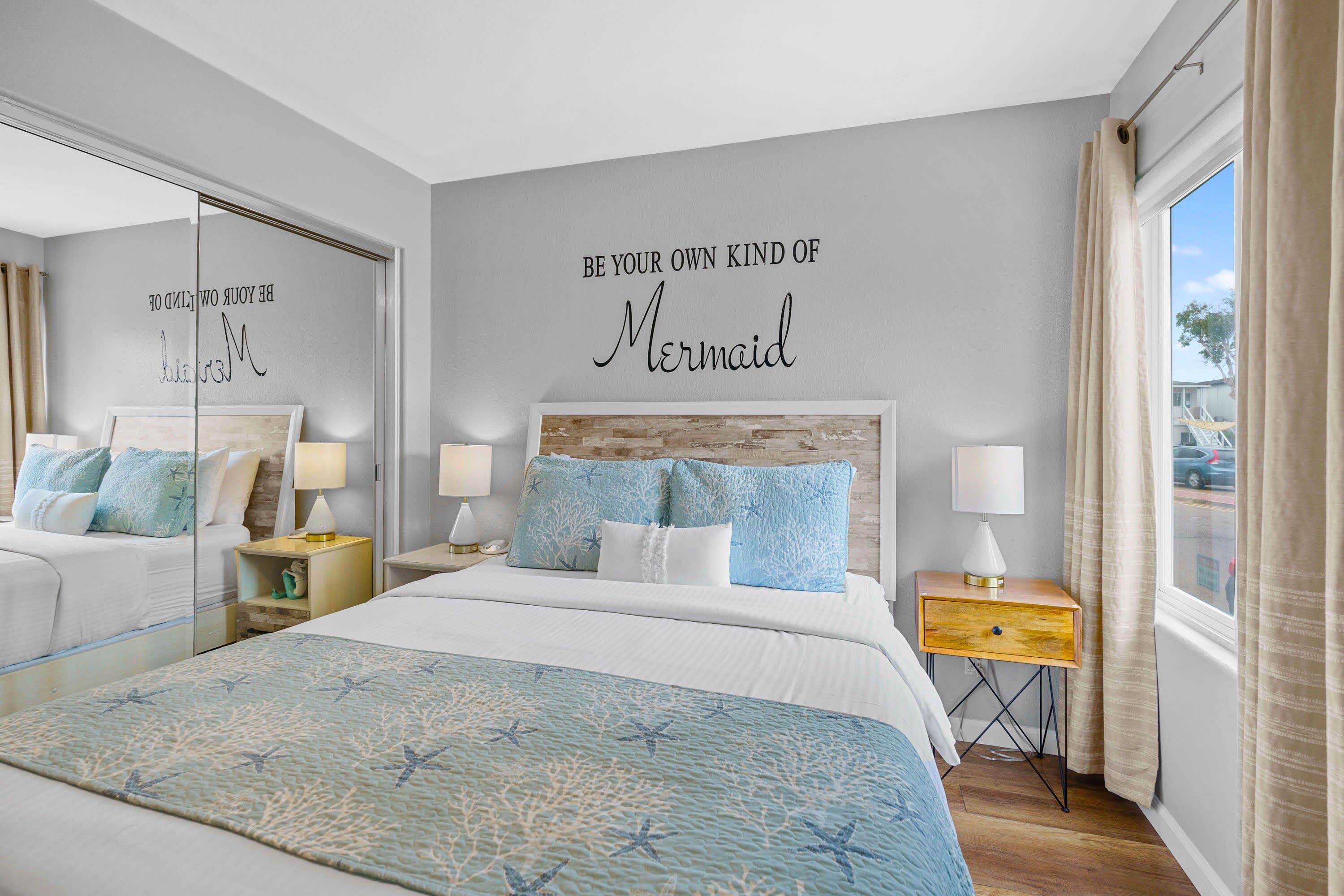 A bedroom with a bed, two bedside tables, a mirror, and a wall with a motivational quote.