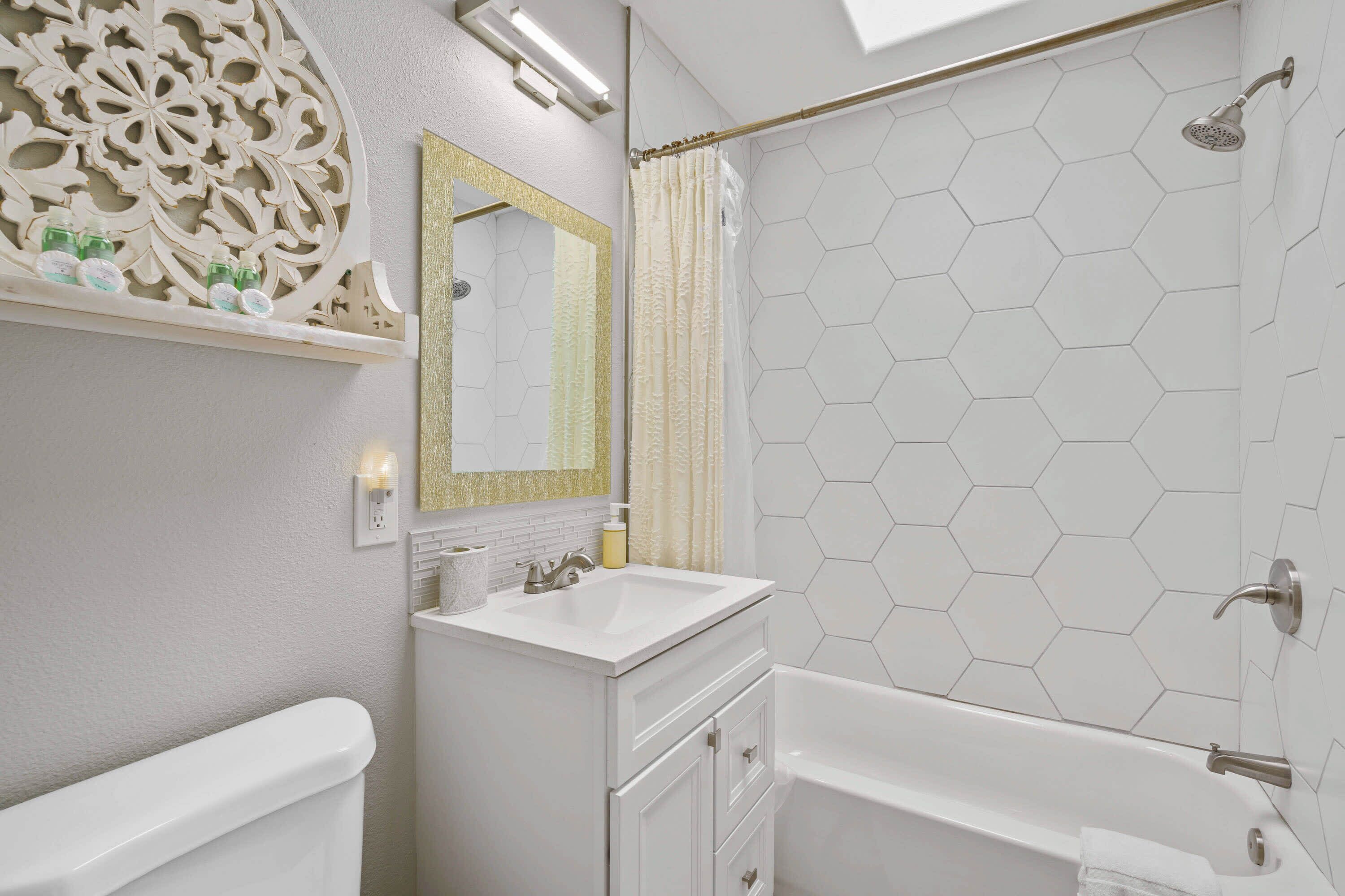 A bathroom with a white vanity, a large mirror, a shower with a hexagonal tile pattern, and a toilet.