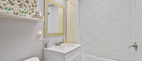 A bathroom with a white vanity, a large mirror, a shower with a hexagonal tile pattern, and a toilet.