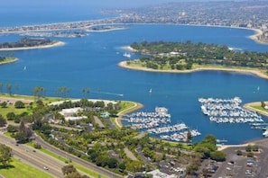 An aerial view of a coastal marina with multiple docks and boats, surrounded by greenery and residential areas. - Beach-2-Bay 2br | Beach | AC | Patio (San Diego)