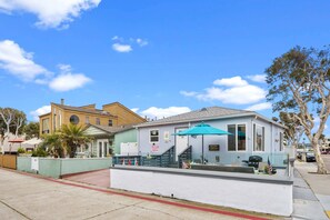 A small, single-story building with a blue awning, a welcome sign, and a patio area. - Beach-2-Bay 2br | Beach | AC | Patio (San Diego)
