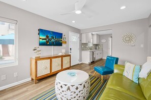 A modern living room with a green sofa, a blue chair, a white round coffee table, and a cityscape painting on the wall. - Beach-2-Bay 2br | Beach | AC | Patio (San Diego)
