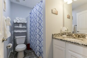 A bathroom with a toilet, a shower curtain, a sink with a mirror, and towels on shelves. - Patriot Place (Branson)