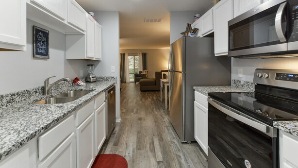 A modern kitchen with white cabinets, granite countertops, stainless steel appliances, and a wood floor.