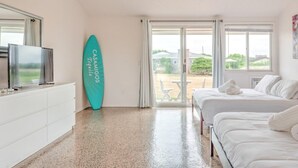 A bedroom with a bed, a TV, a surfboard, and a view of the outdoors. - Unit 8 King - Bungalows at Common Ground (Montauk)