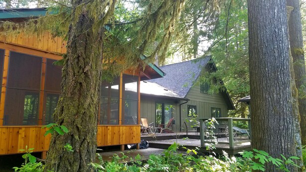 A cabin with a wooden deck, surrounded by trees and a covered porch.