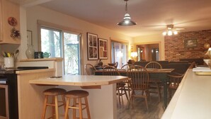 A kitchen with a central island, wooden chairs, a dining table, and a brick wall.