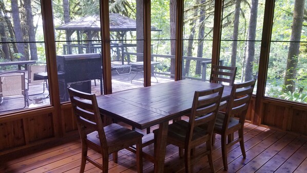 A wooden deck with a table and chairs, large windows, and a gazebo in the background.
