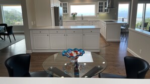 Une cuisine moderne avec des meubles blancs, un îlot central et un coin repas doté d’une table en verre.
