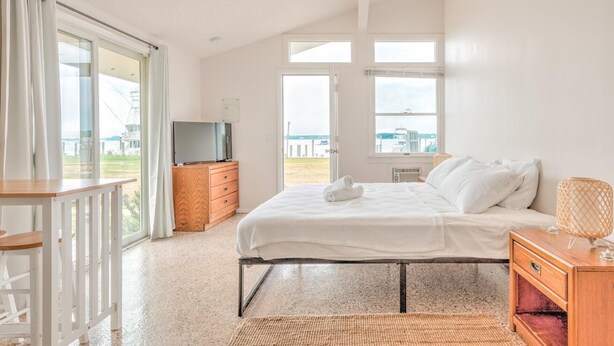 Un dormitorio con cama, televisor, cómoda de madera y vista al exterior.