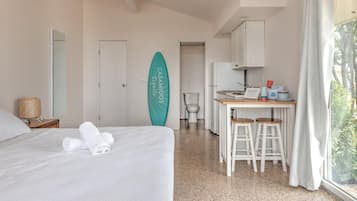 Quarto de hotel com cama, banheiro, cozinha compacta e vista para árvores.