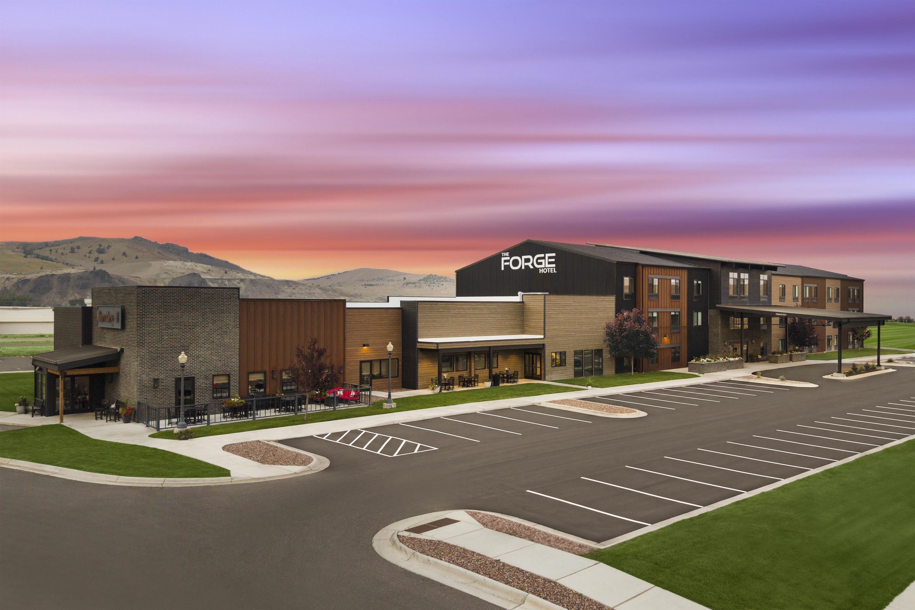 A hotel with a modern design, a parking lot, and a view of the mountains in the background.