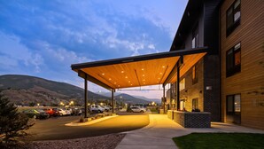 Un bâtiment moderne doté d’une entrée couverte, d’un parking et surplombant un paysage montagneux.