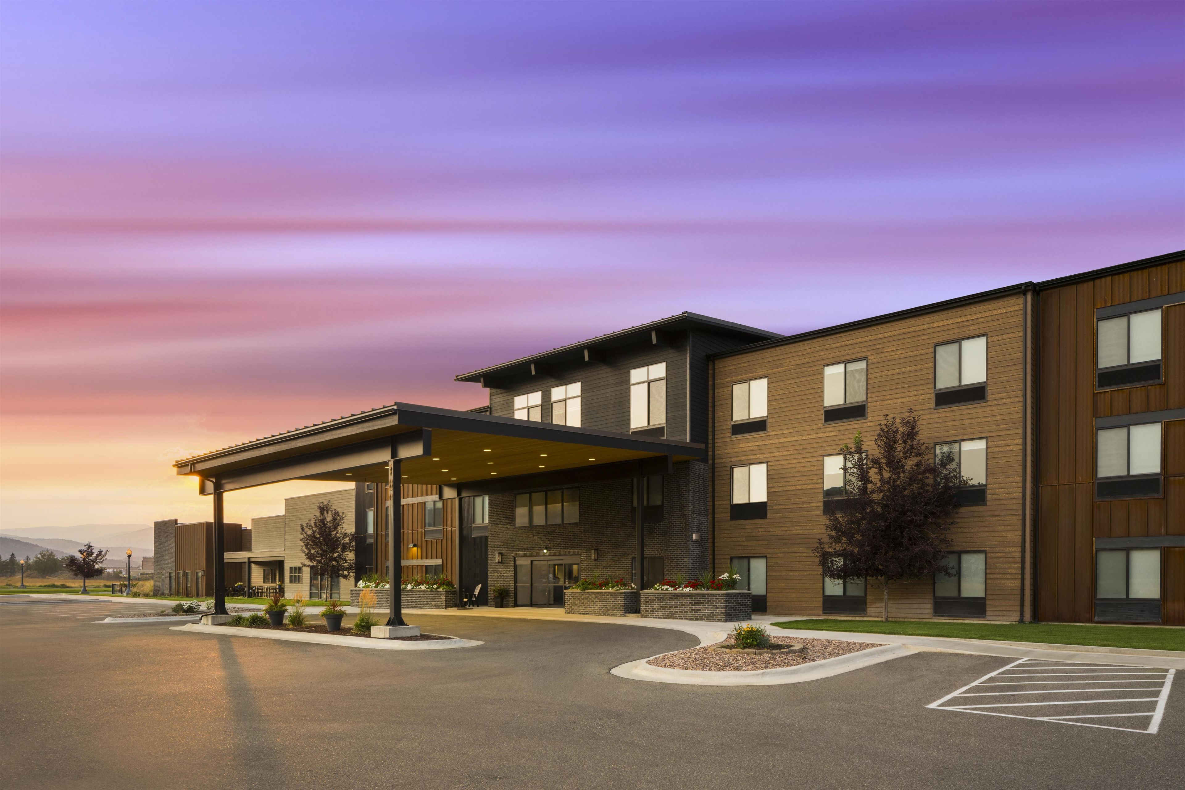 A modern building with a covered entrance, multiple windows, and a parking lot.