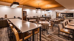 Un hall d’hôtel moderne doté d’un long comptoir d’accueil, de plusieurs espaces salon et d’une petite cuisine.