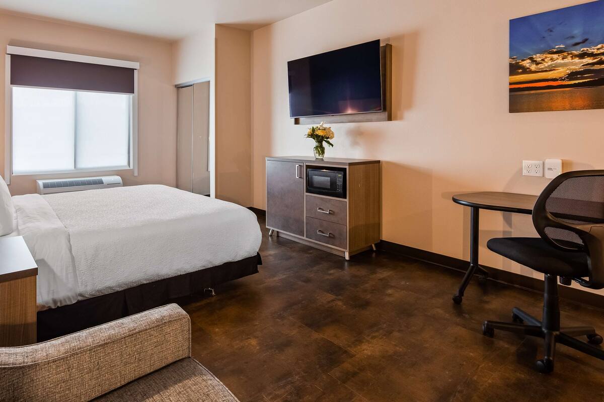 Una habitación de hotel con cama, escritorio, silla, televisor y armario.