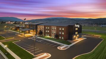 A hotel with a parking lot and a view of the mountains in the background.