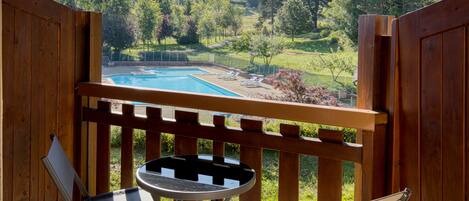 A wooden deck with a pool, two lounge chairs, and a small table.