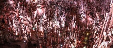 A cave with stalactites and stalagmites, illuminated by artificial lighting.