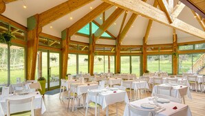 Un vaste espace de restauration intérieur, doté de nombreuses tables et chaises, de grandes fenêtres et de poutres en bois.