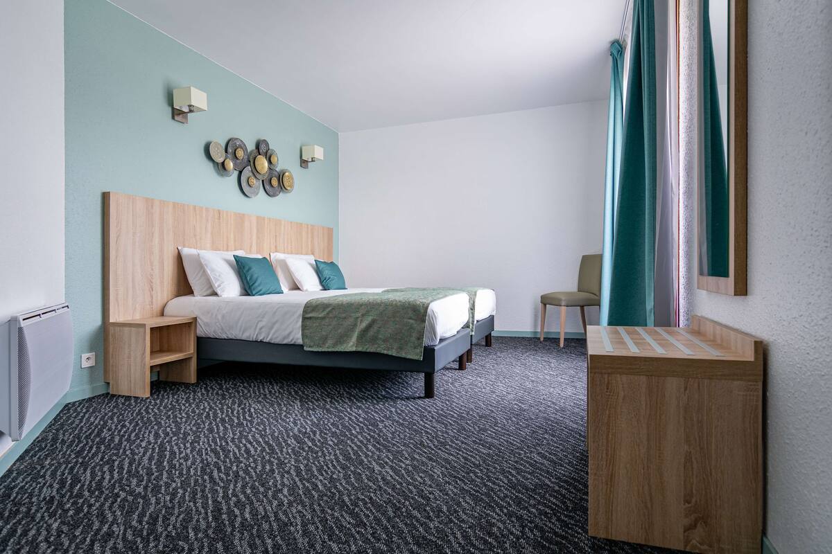 Een hotelkamer met een bed, nachtkastje, stoel, klein houten kastje en een wandlamp.