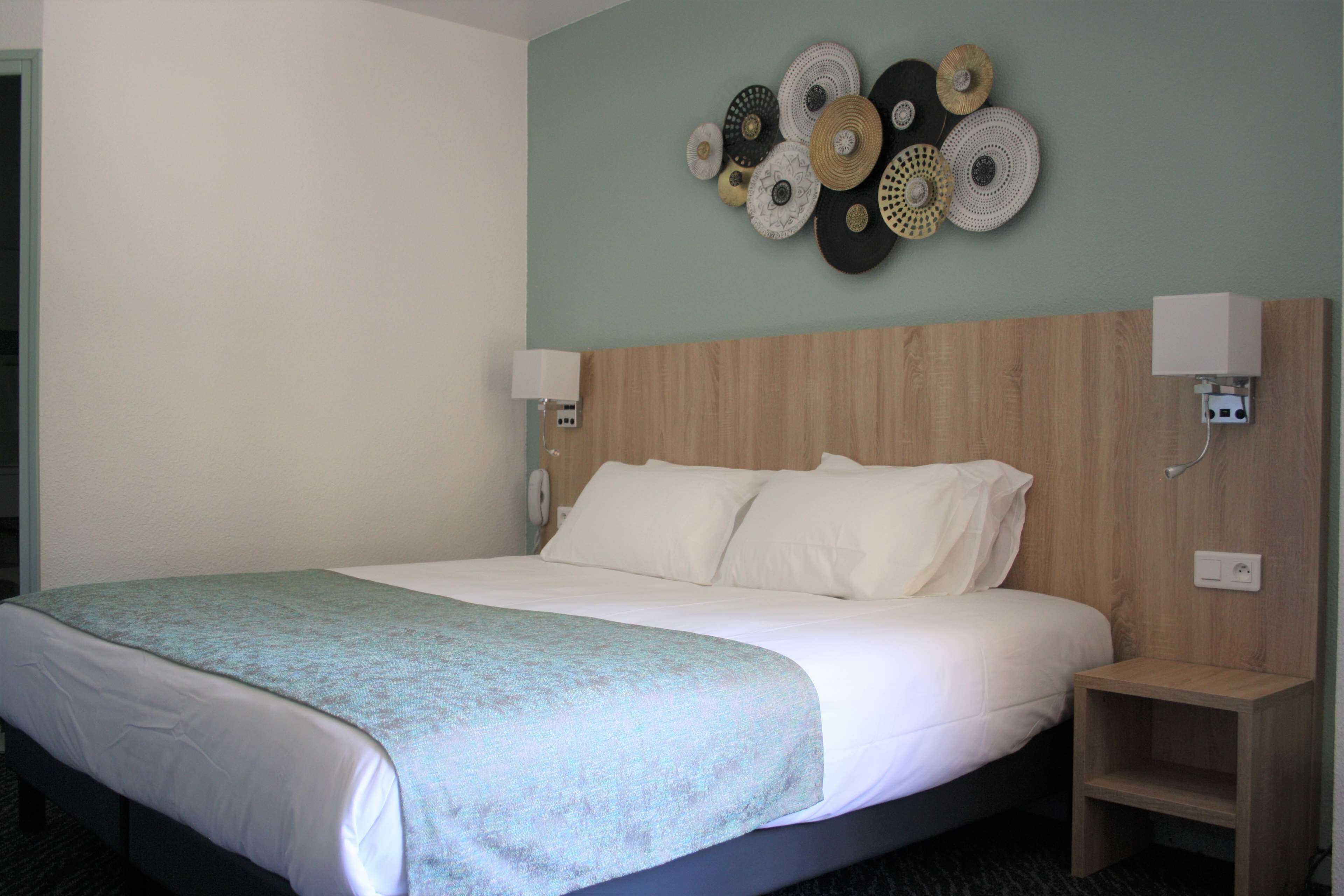 Une chambre d’hôtel comprenant un lit, une table de chevet, une lampe fixée au mur et un élément décoratif mural.