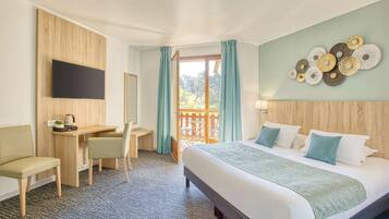 Una habitación de hotel con cama, escritorio, silla y televisor montado en la pared.