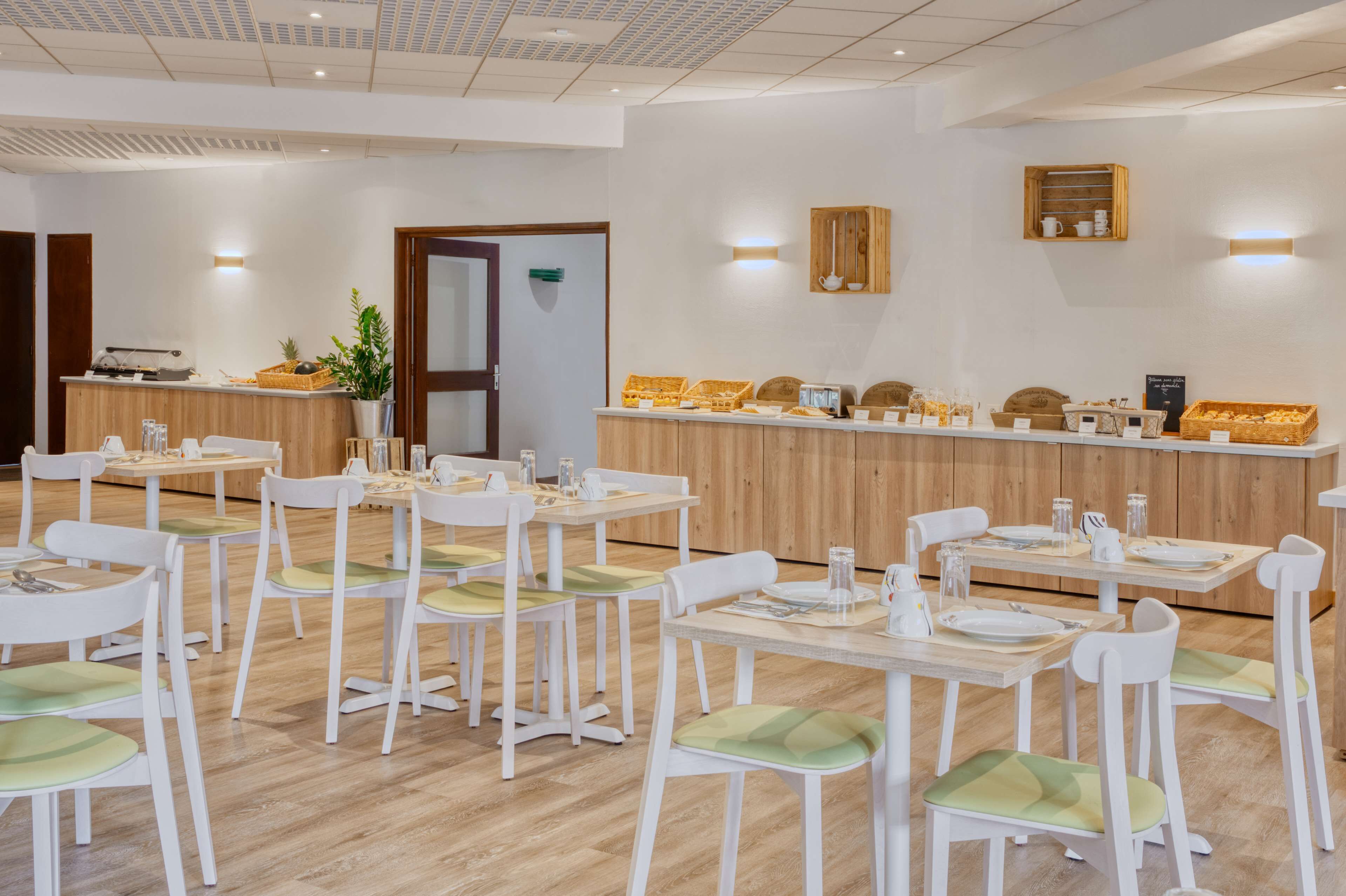Een eetgedeelte met witte stoelen en tafels, een houten toonbank met etenswaren, en een potplant.
