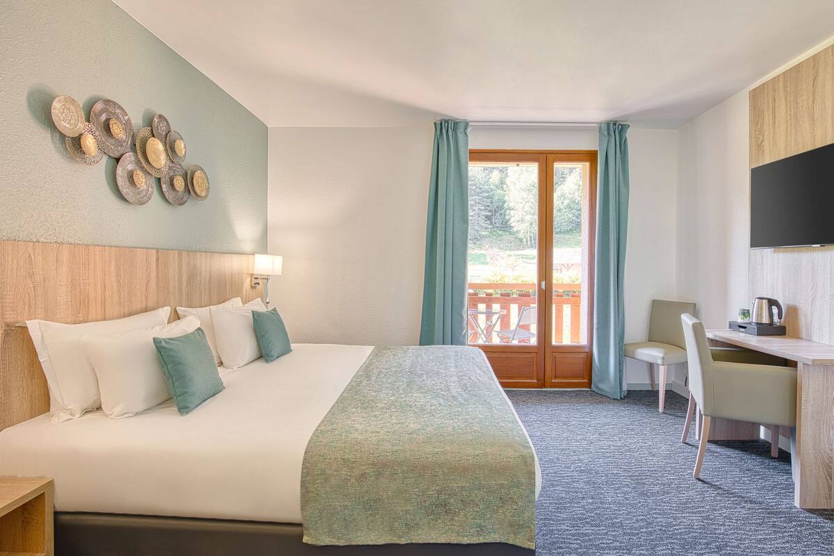 Een hotelkamer met een bed, bureau, stoel en een balkon met gordijnen.