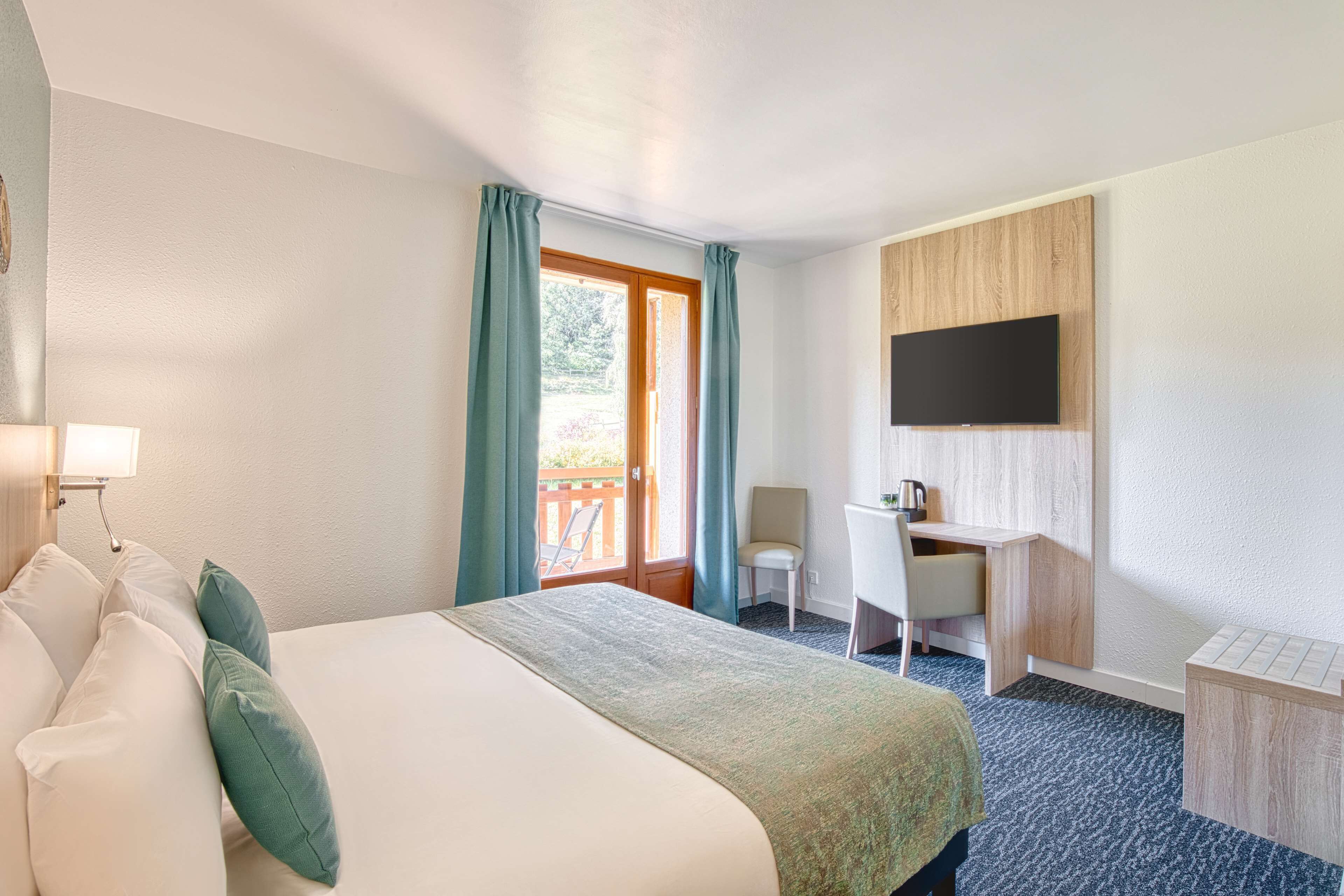 A hotel room with a bed, a desk, a chair, a TV, and a balcony.