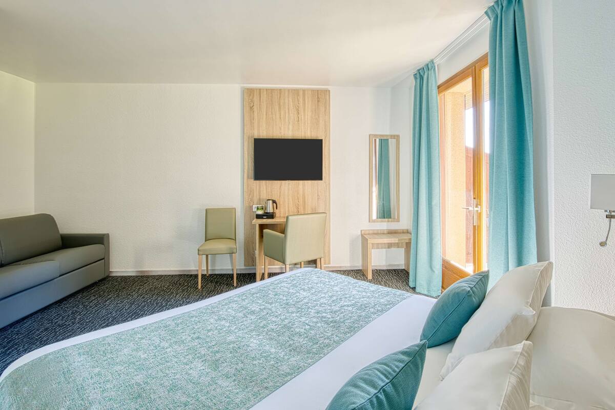 Hotelkamer met een bed, bureau, stoel, bank, televisie en deur naar de badkamer.